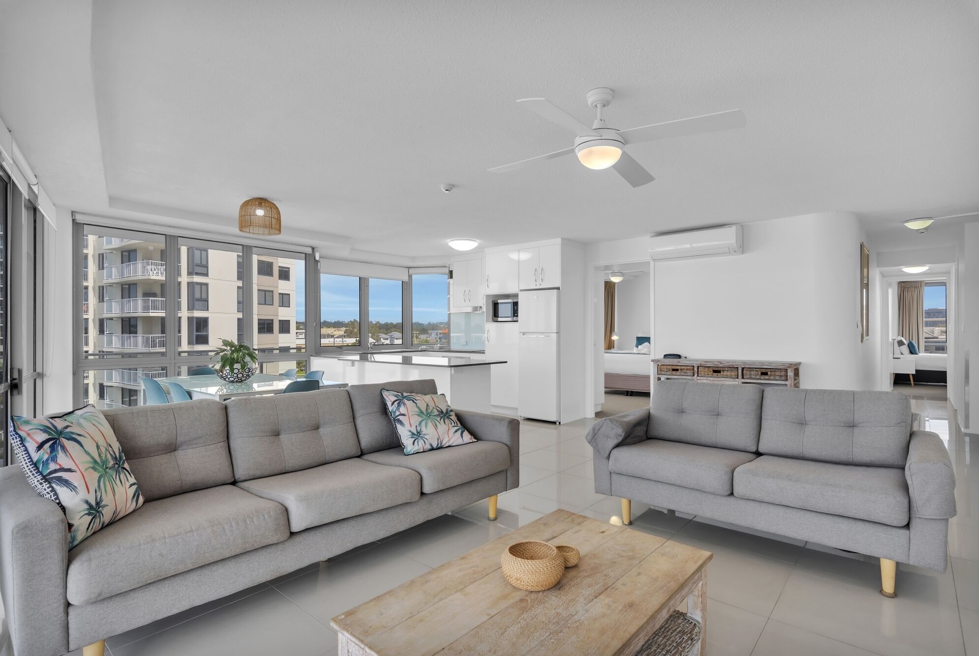 A modern apartment with two grey sofas, a wooden coffee table, and a ceiling fan.