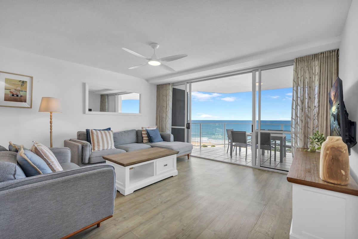 A spacious living area with a sofa, coffee table, and a television on a stand.