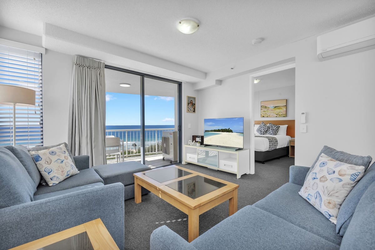 A modern hotel room with a balcony, a TV, a bed, and a seating area with a glass coffee table.