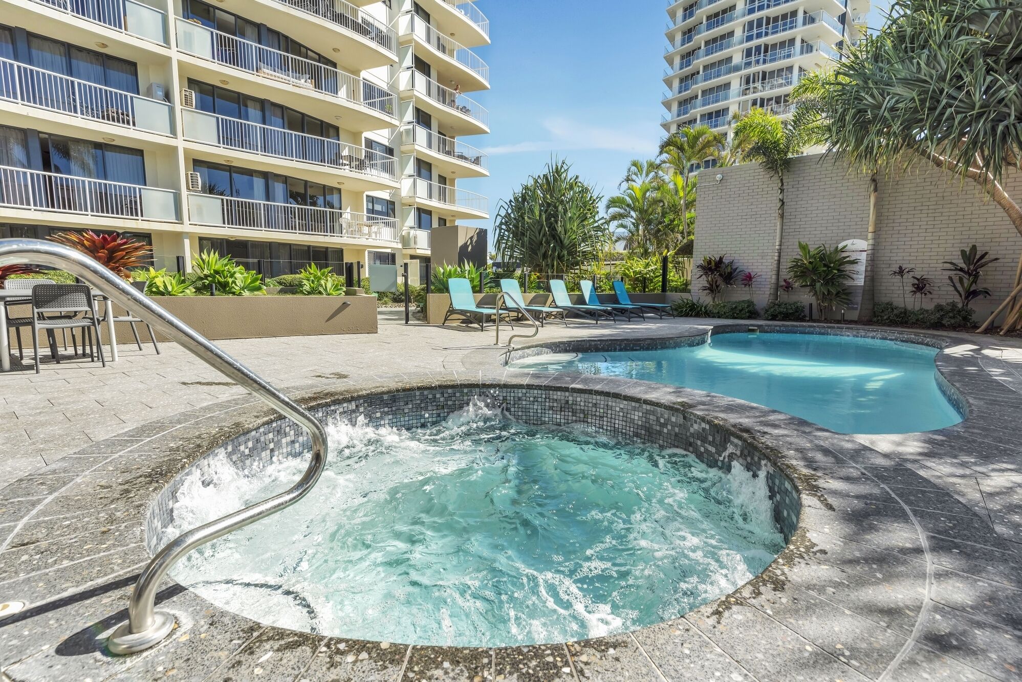 Een zwembadgedeelte van een hotel met een jacuzzi, ligbedden en een gebouw met balkons.