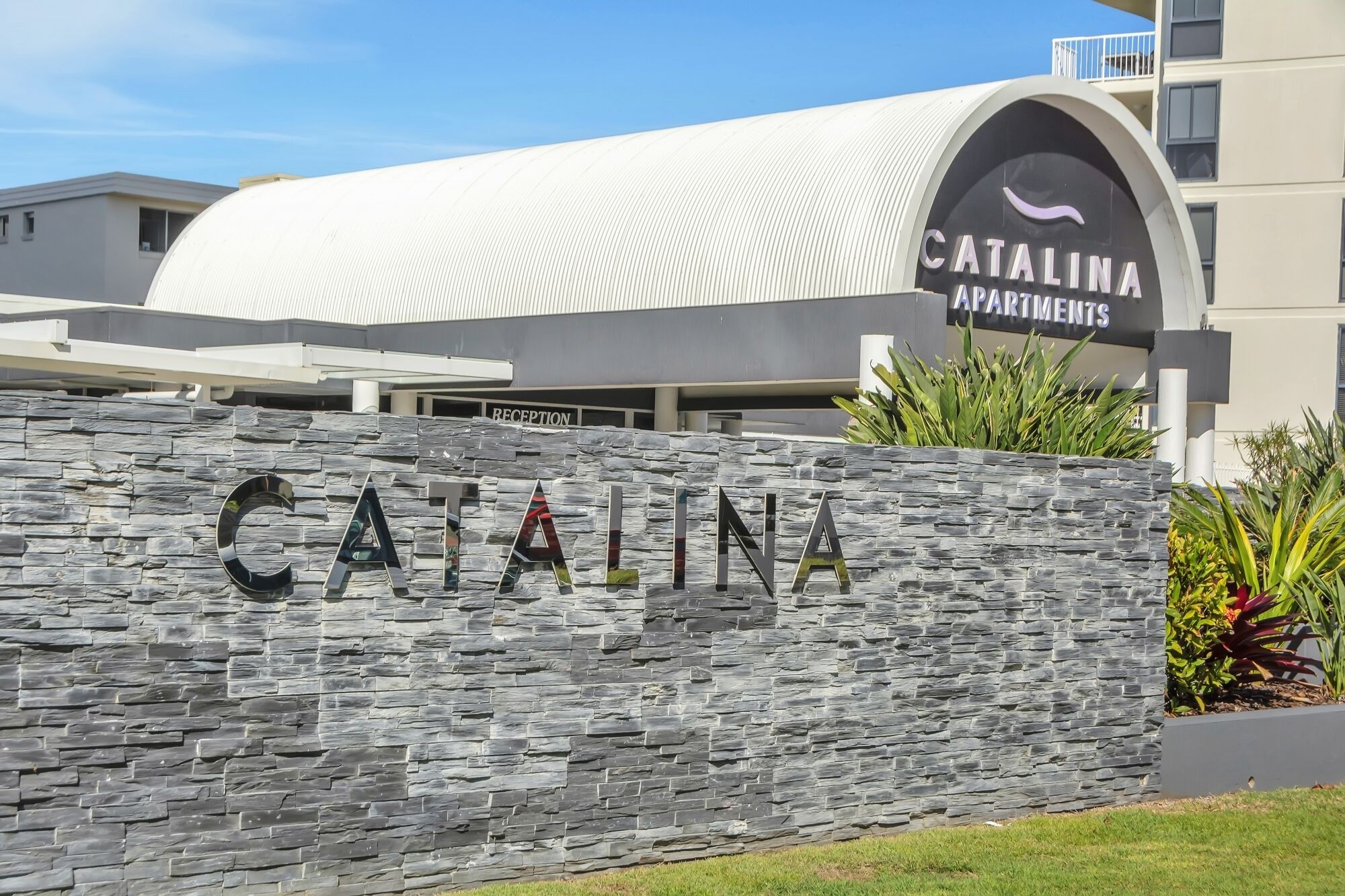 A stone wall with the name 'Catalina Apartments' and a modern building in the background.