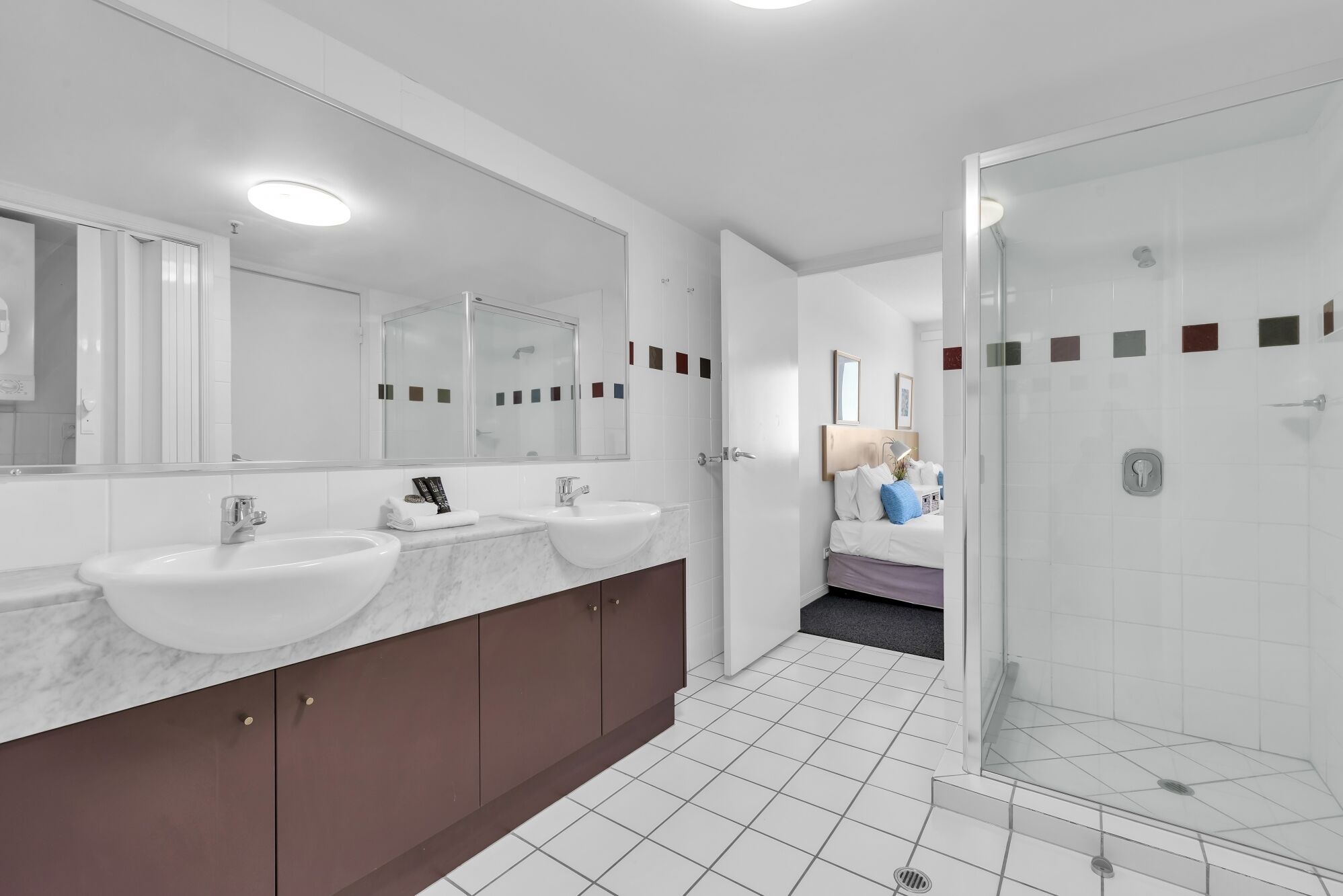 Une salle de bain moderne avec deux lavabos, un grand miroir et une douche à l’italienne.