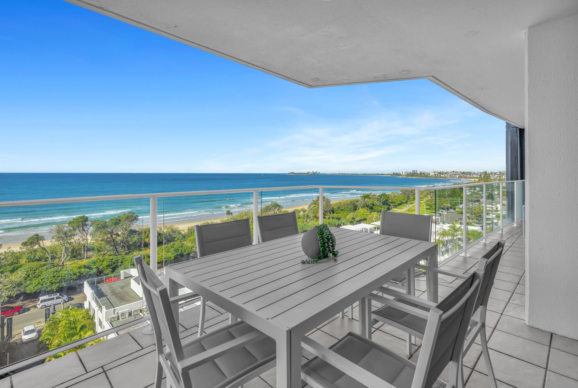 A balcony with a table and chairs, overlooking a beach and ocean.