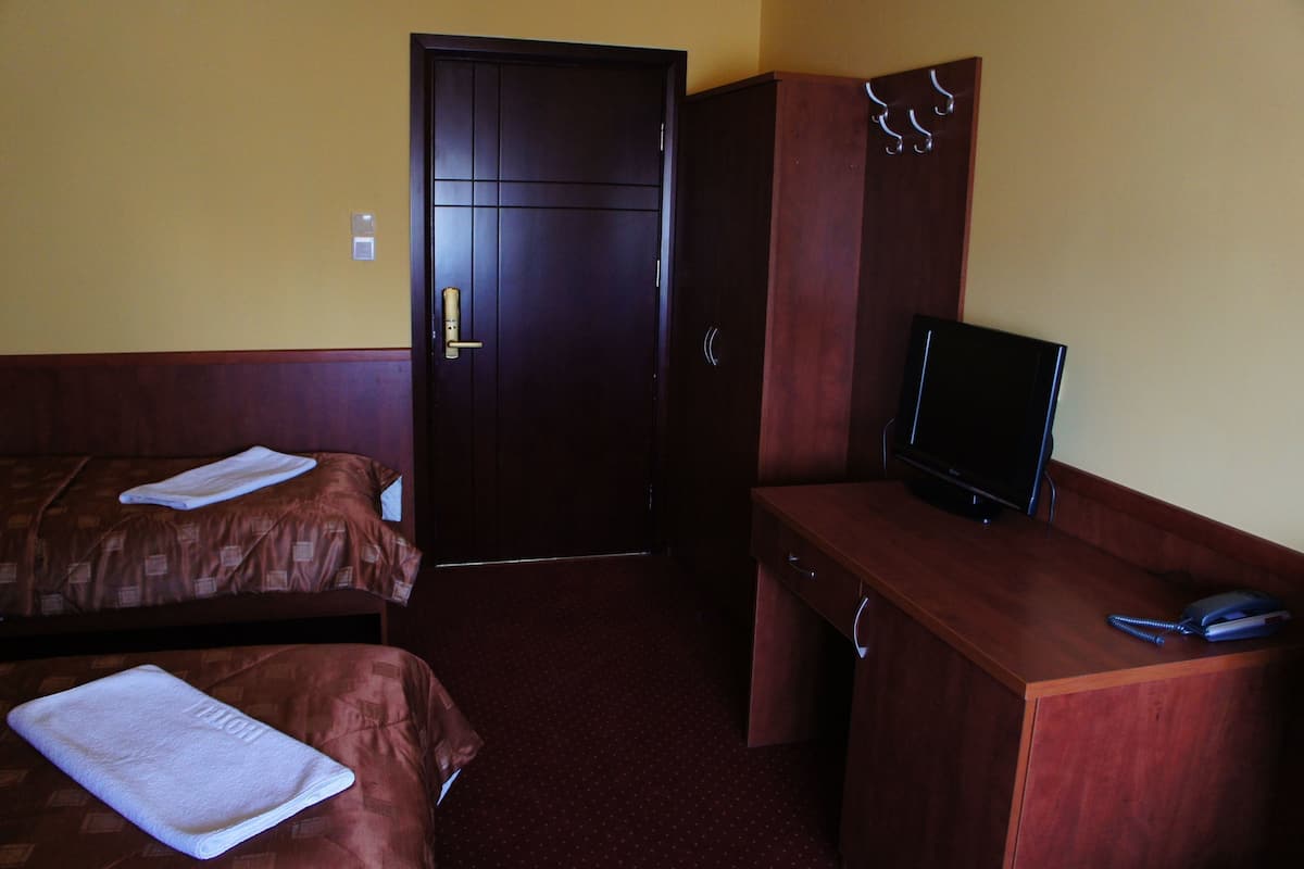 Quarto de hotel com duas camas, uma escrivaninha com televisão e um guarda-roupa.