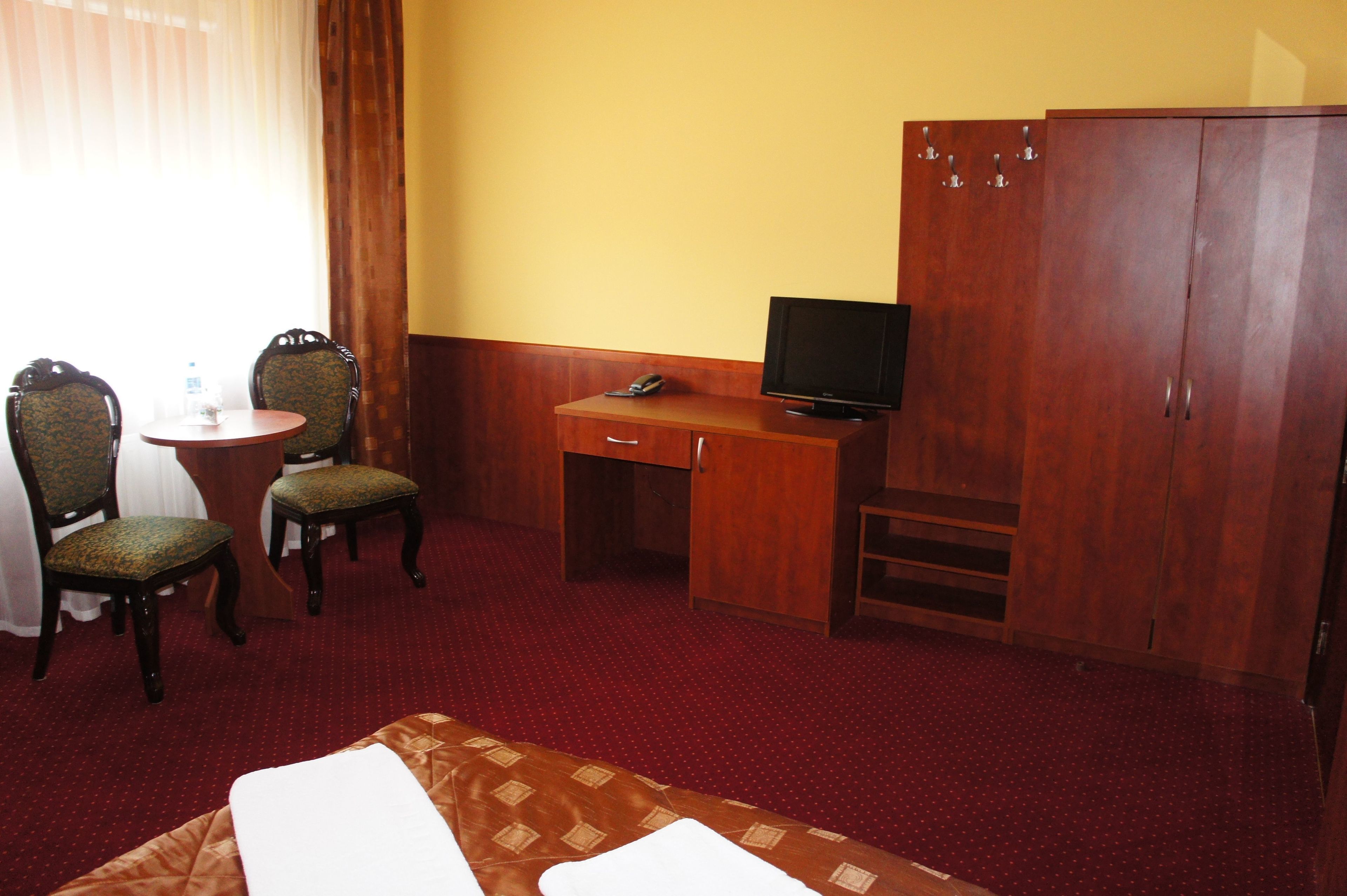 A hotel room with a bed, a desk with a television, two chairs, and a wardrobe.