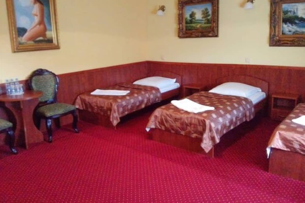 Quarto de hotel com duas camas de solteiro, uma cadeira de madeira, uma pequena mesa com uma garrafa de água e três quadros nas paredes.