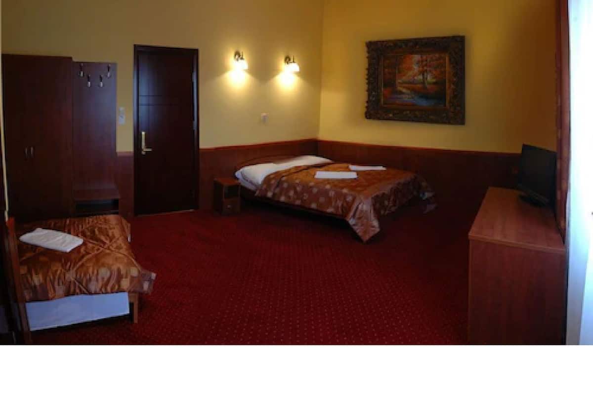 Quarto de hotel com uma cama, uma cadeira, uma escrivaninha e um quadro na parede.