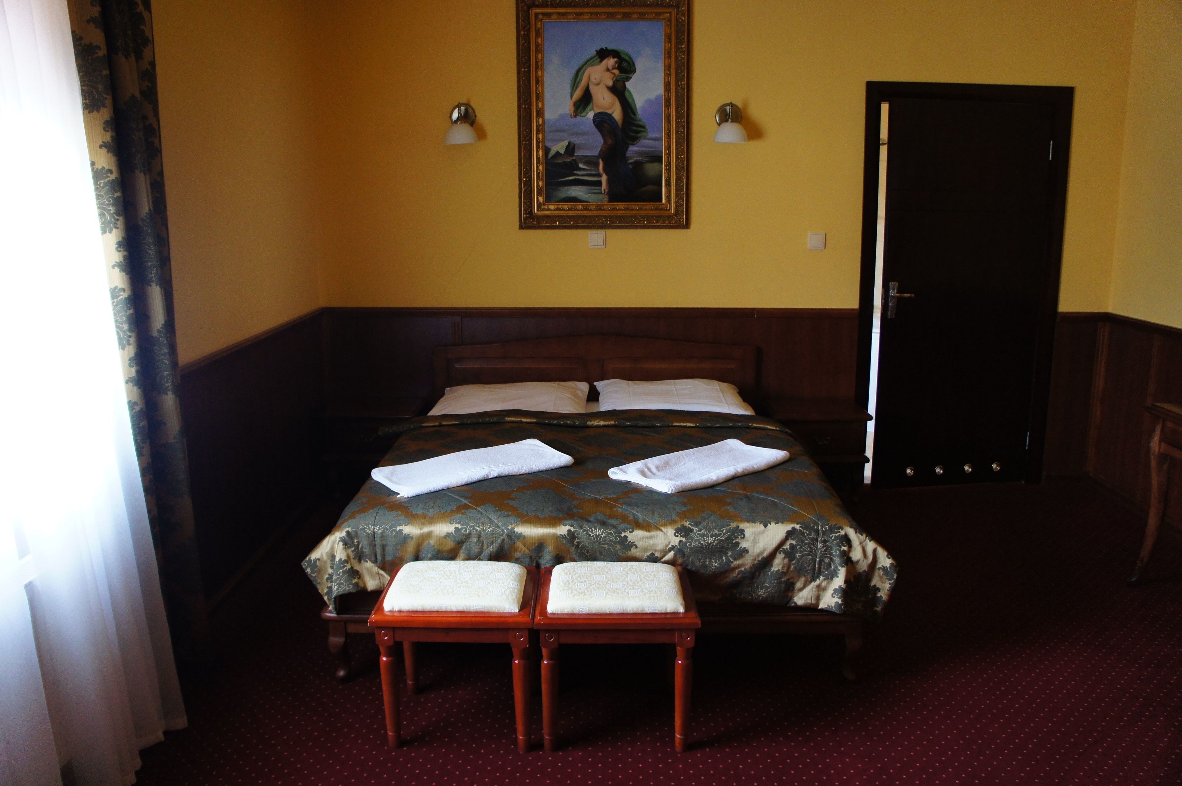 A hotel room with a bed, two bedside tables, a painting on the wall, and a door.