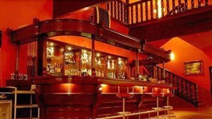 A bar area with a curved wooden counter, stools, and a staircase leading to an upper level. - Dobosz (Police)