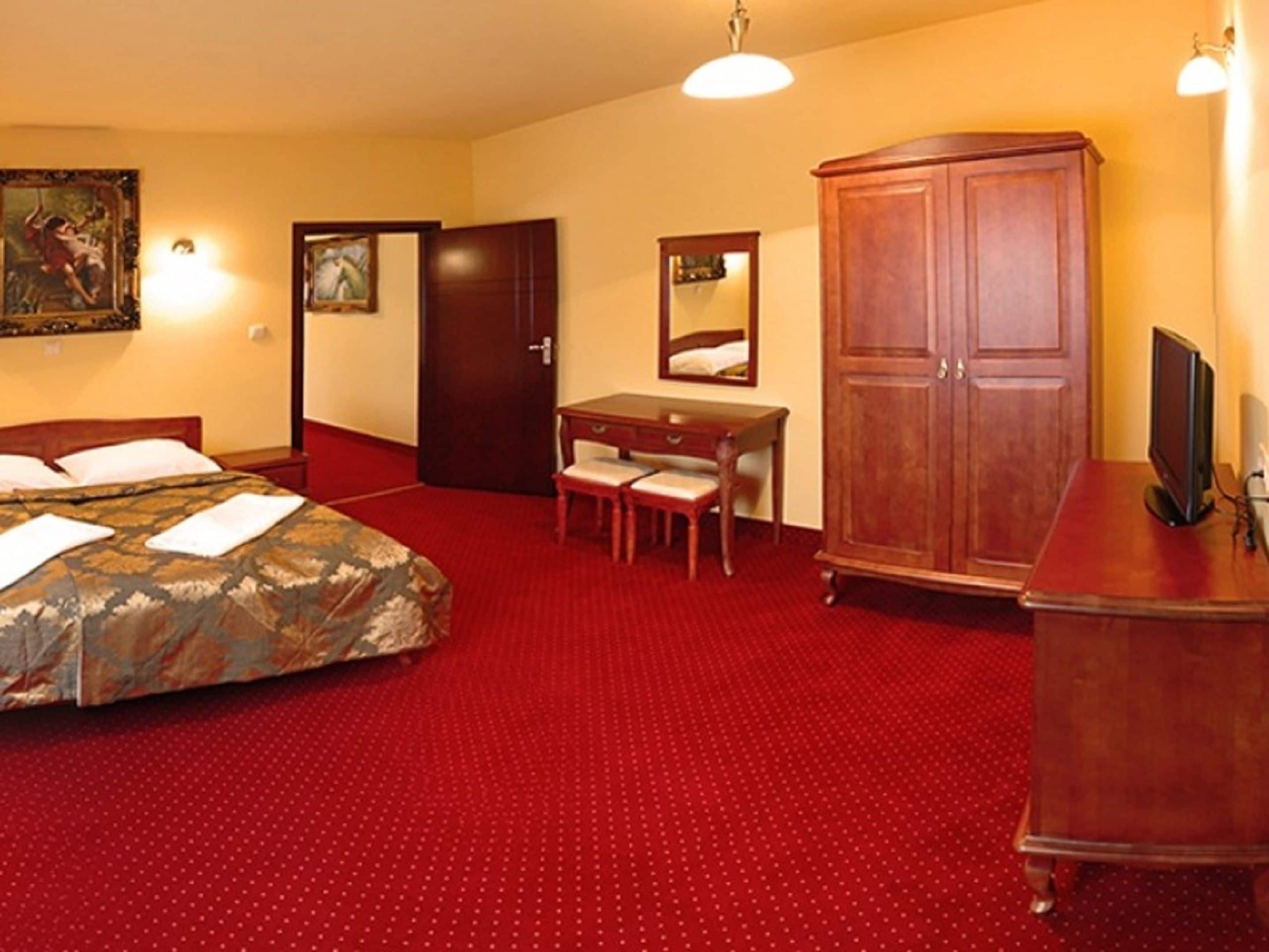 Quarto de hotel com cama, escrivaninha, cadeira, guarda-roupa e televisão.