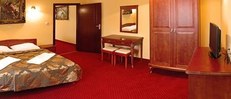 Quarto de hotel com cama, escrivaninha, cadeira, guarda-roupa e televisão.