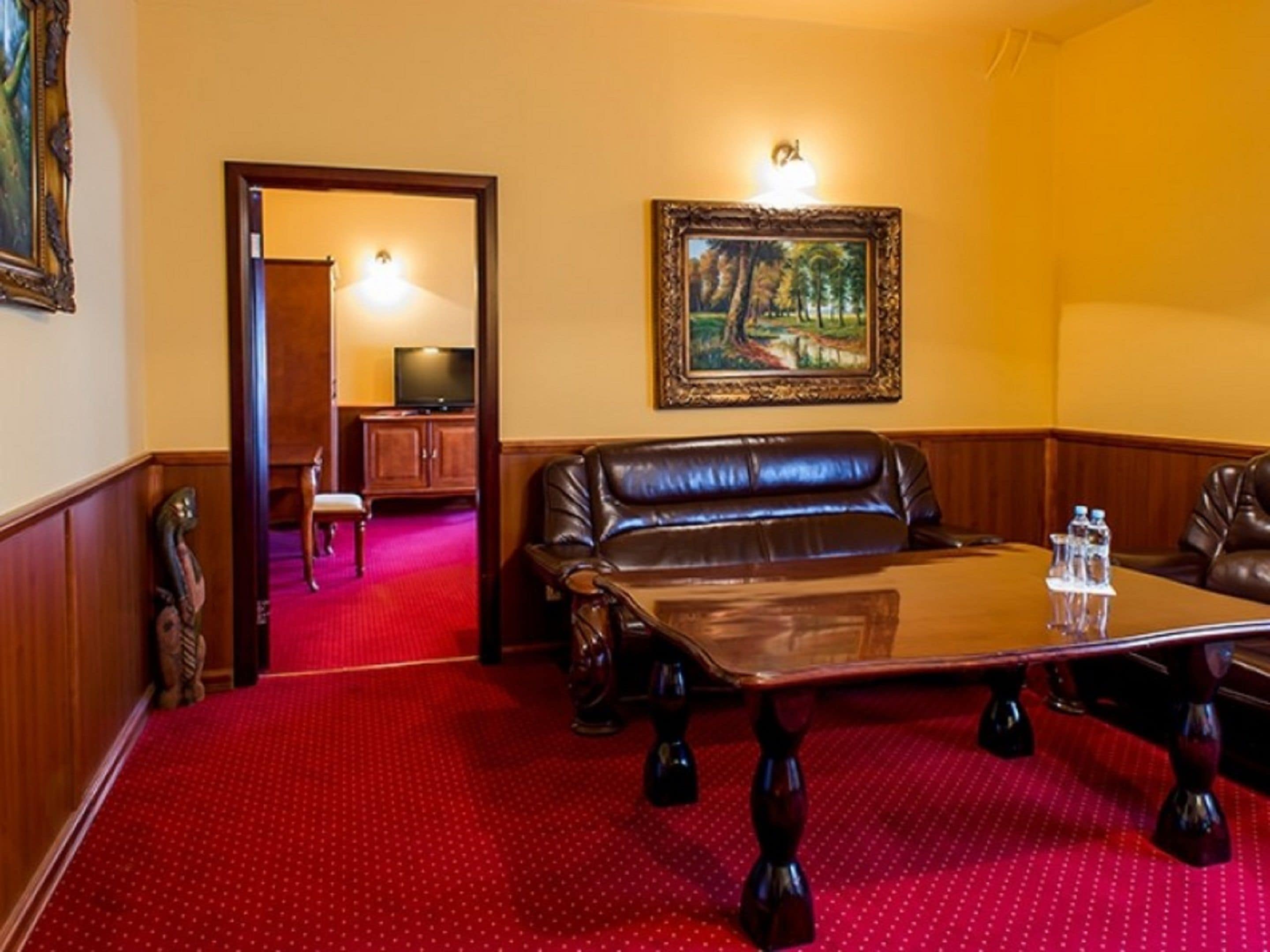 A conference room with a red carpet, a brown leather sofa, a glass table, and a painting on the wall.