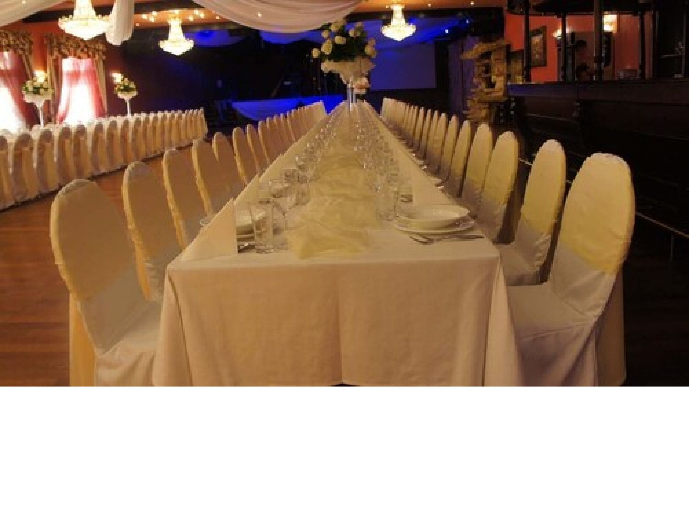 A long banquet table set with white tablecloths and chairs, centered with a floral arrangement.
