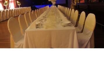 A long banquet table set with white tablecloths and chairs, centered with a floral arrangement.