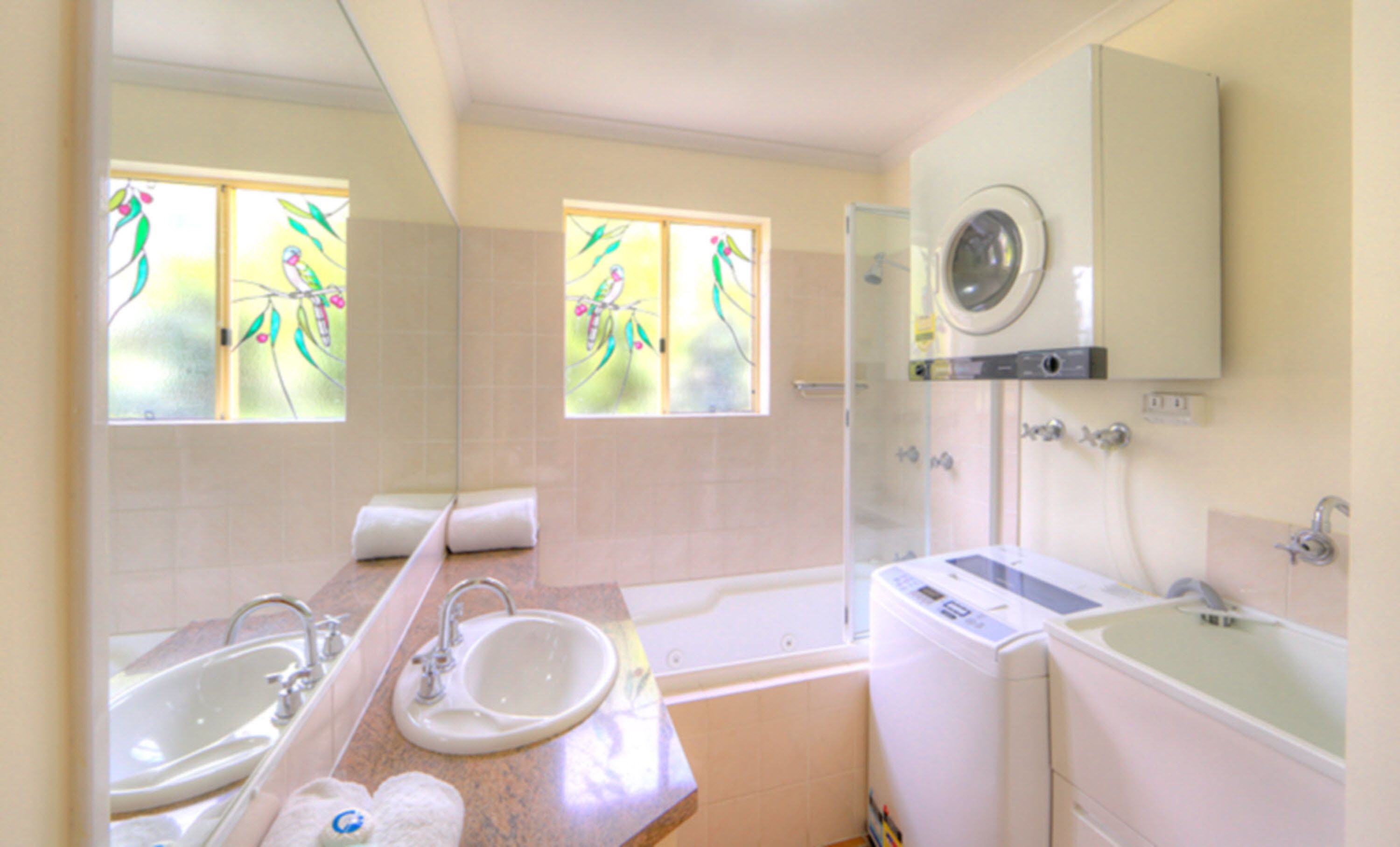A bathroom with two sinks, a bathtub, a washing machine, and a window with a floral view.