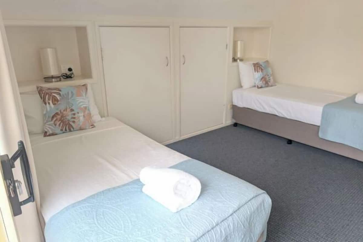 A room with two beds, a wardrobe, a shelf with a lamp, and a small table with a cup.