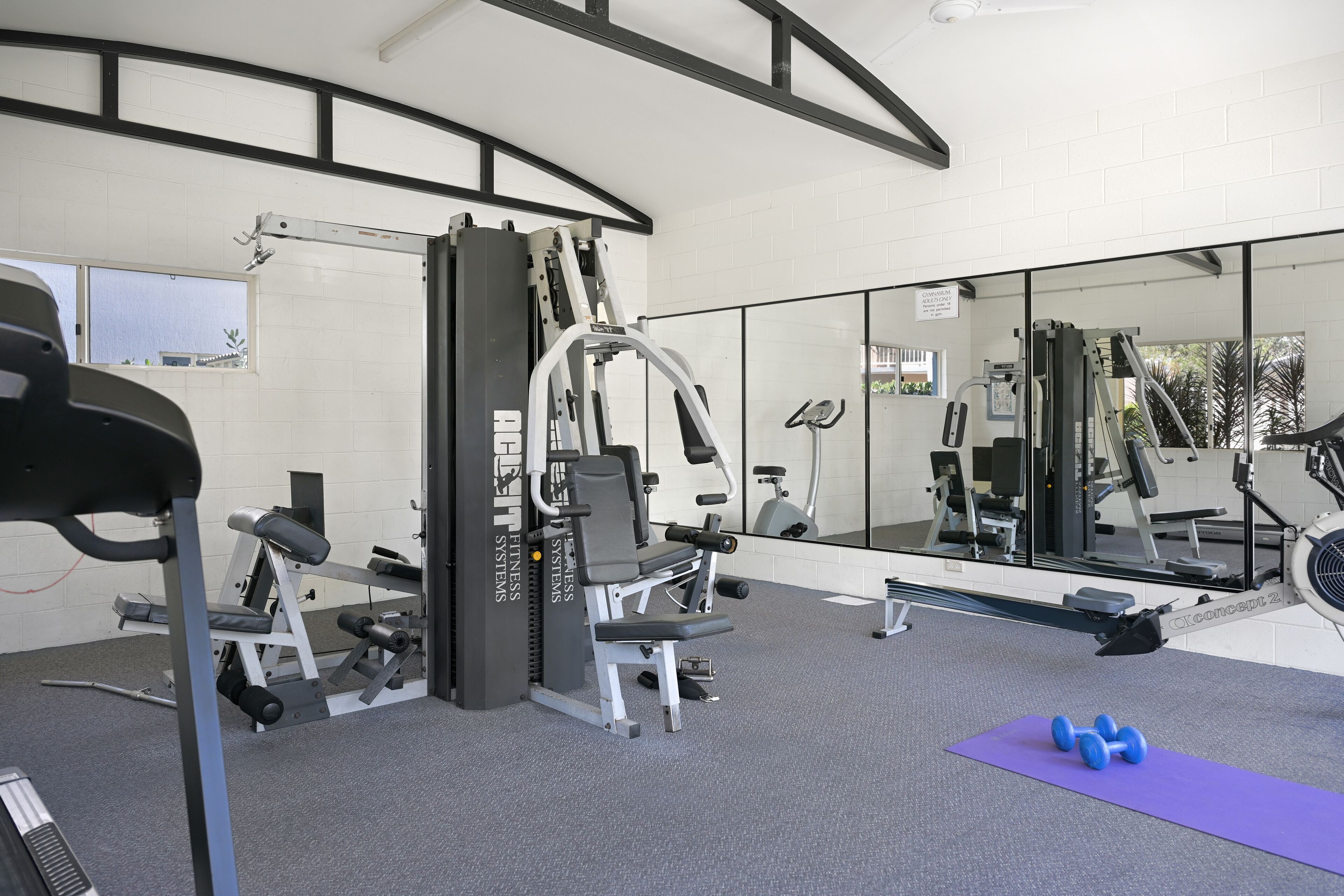 Une salle de sport équipée de matériel d’exercice, d’un miroir et d’un tapis violet.