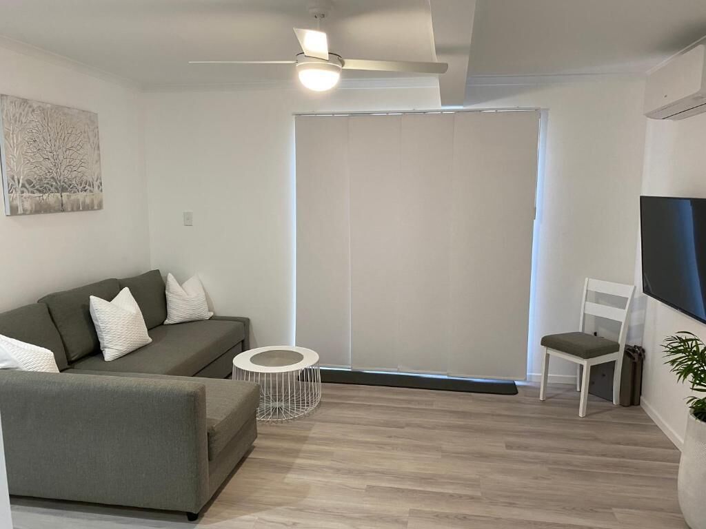 A modern living room with a grey sofa, a white chair, a small round table, and a ceiling fan.