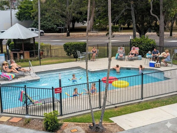 Piscina con zona vallada, sillas de descanso y pabellón sombreado.