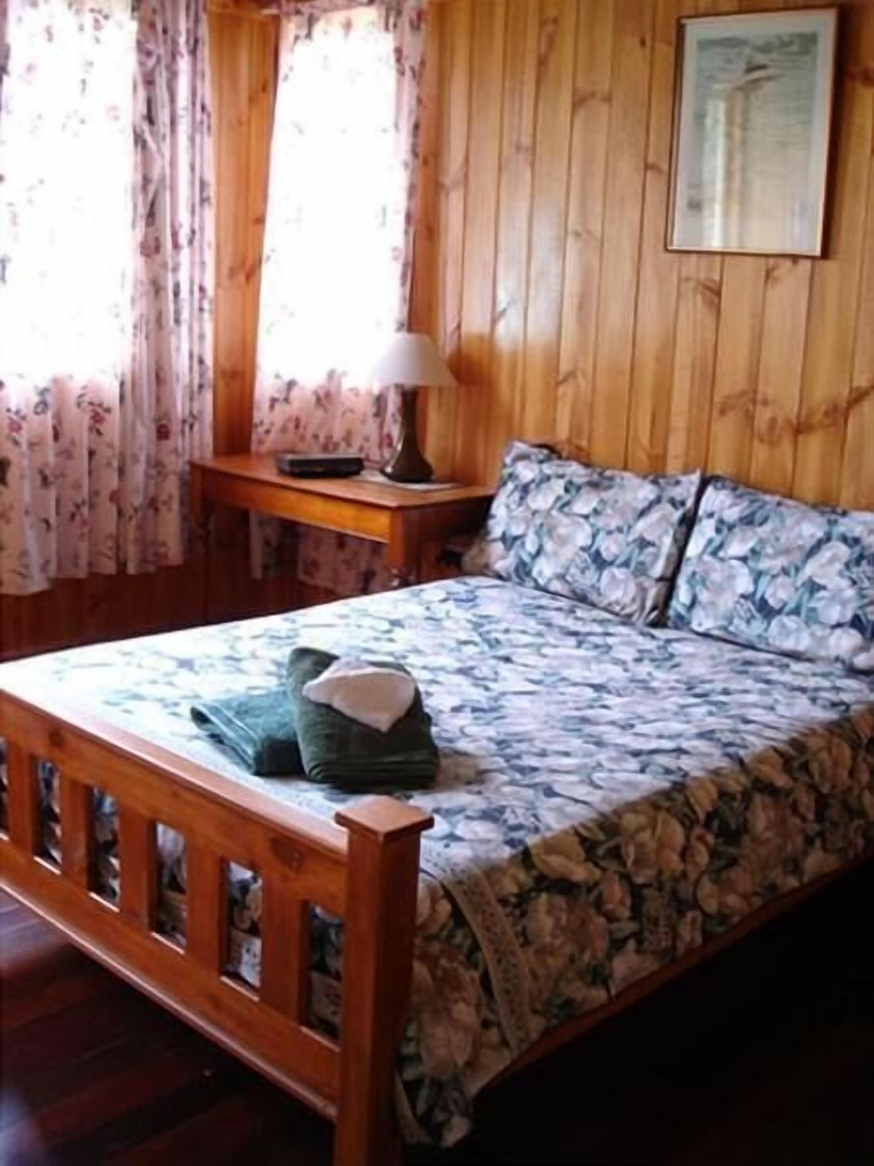Una habitación con paneles de madera, una cama, una mesita de noche y una lámpara.