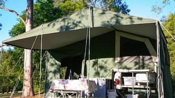 A large, green tent with a table and chairs set up inside, surrounded by trees.