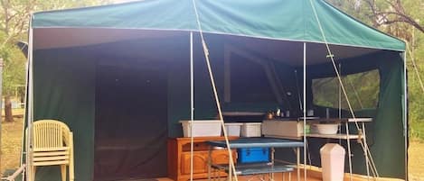 A green tent with a table and chairs set up outside.