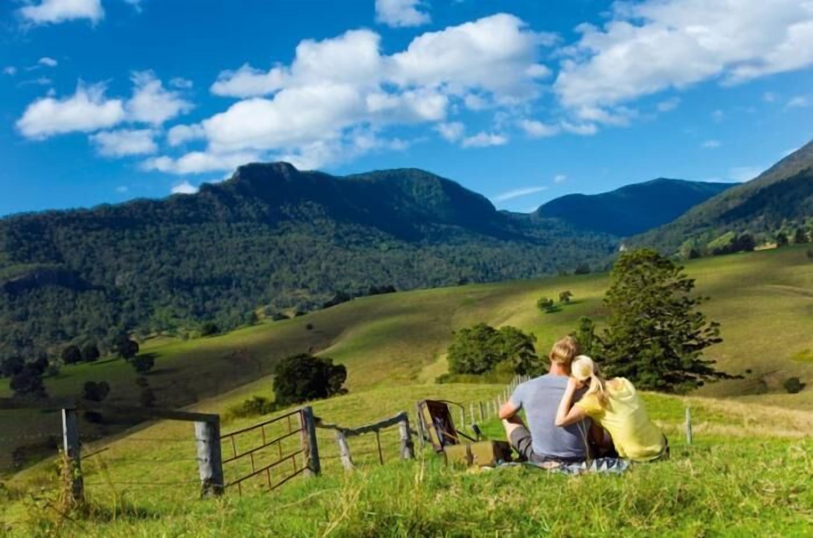 A couple sitting on a blanket in a grassy field with a mountain backdrop.