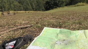 A map, compass, and notebook on grass with mountains in the background.