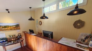 A reception desk with a wooden finish, two pendant lights, a framed landscape painting, and a wall clock. - Mt Barney Lodge Country Retreat (Mount Barney)