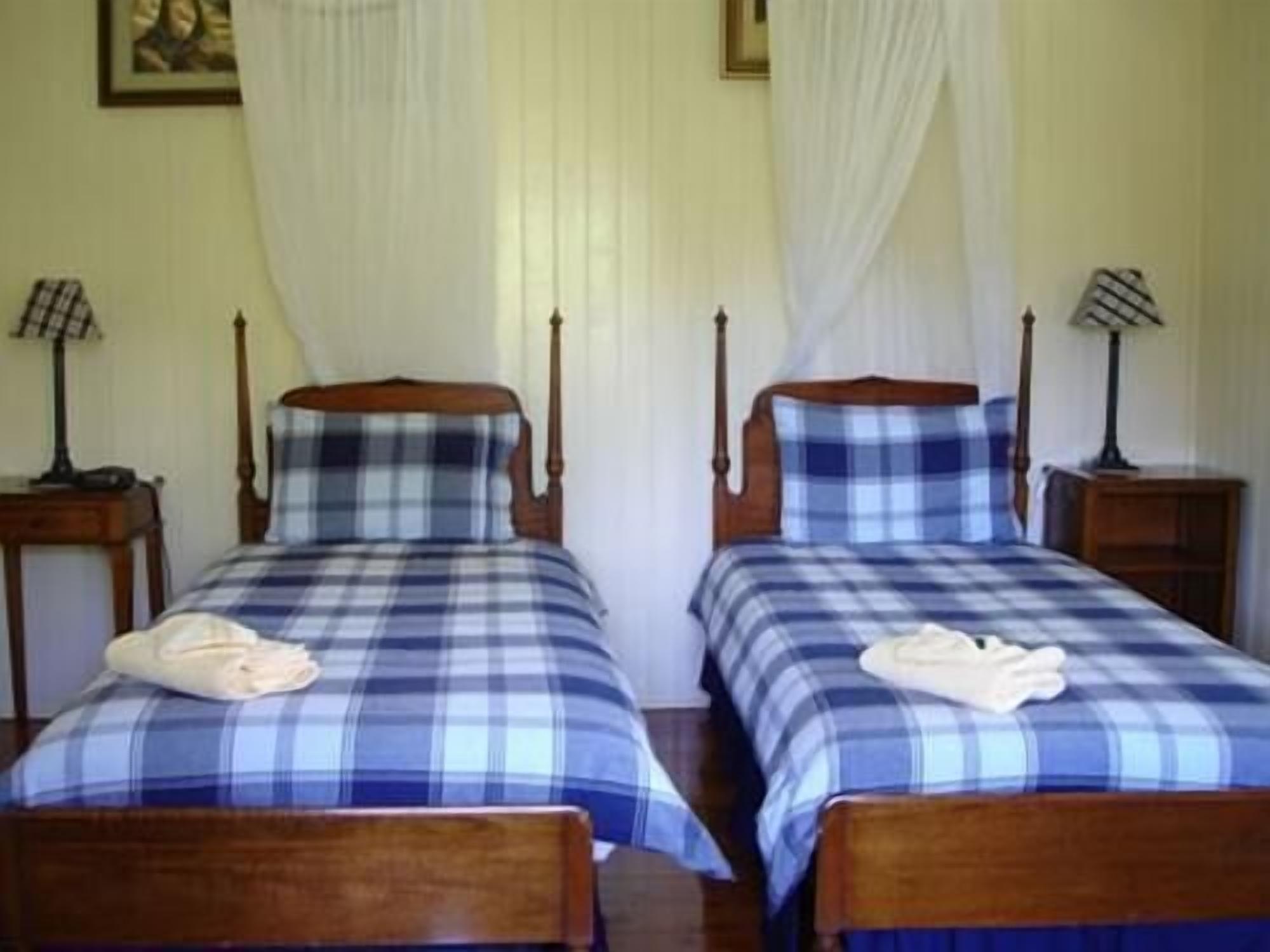 Two twin beds with wooden headboards and blue plaid bedding. Each bed has a bedside table with a lamp.
