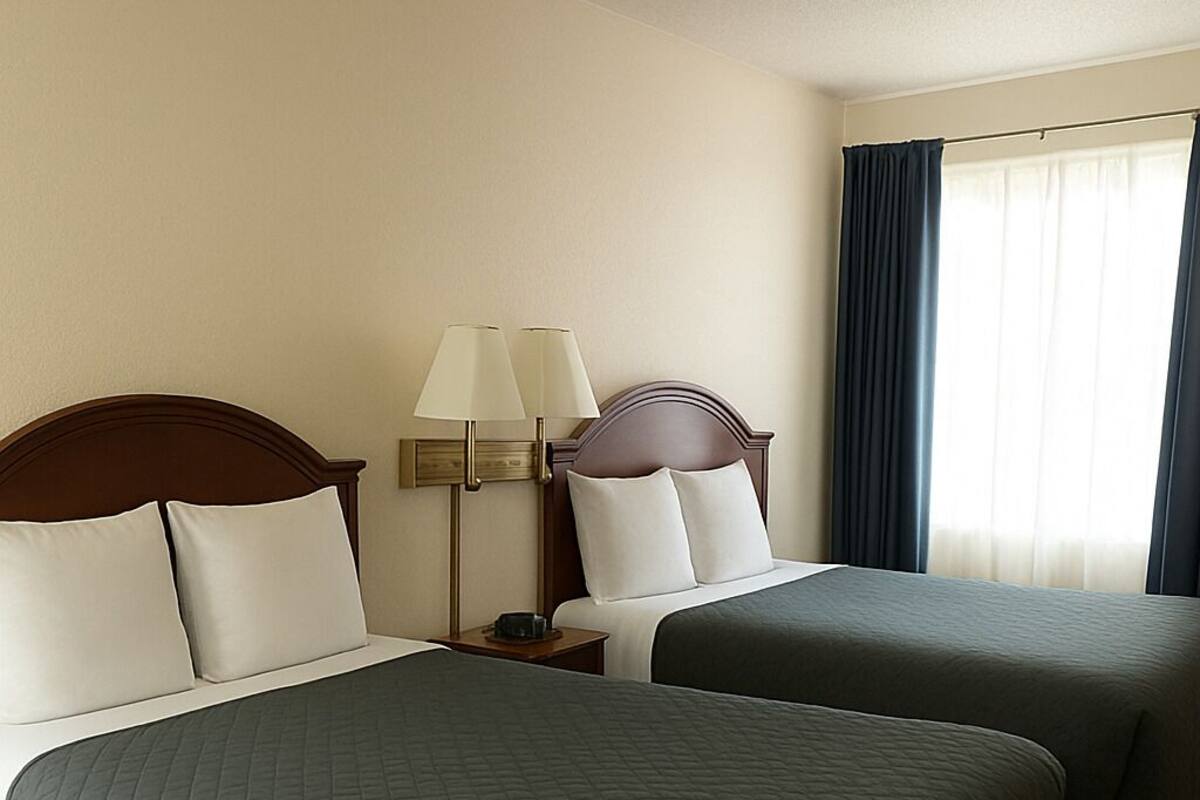 A hotel room with two beds, a nightstand with lamps, and a window with curtains.