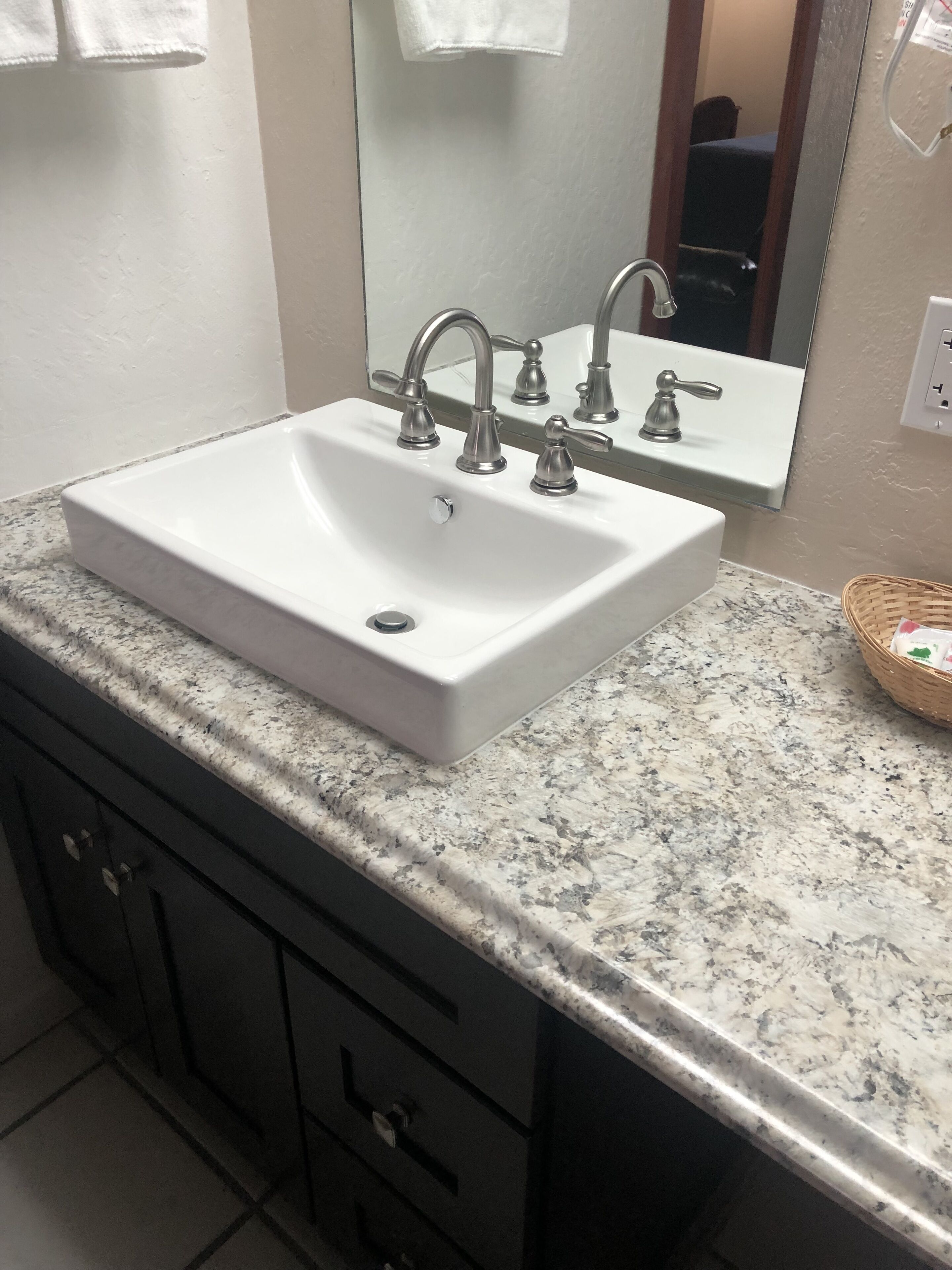 A bathroom with a white sink, three faucets, a mirror, and a granite countertop.