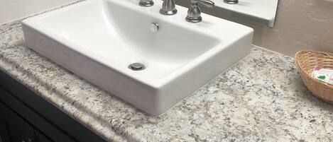 A bathroom with a white sink, three faucets, a mirror, and a granite countertop.