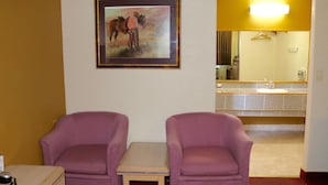 A hotel room with two purple armchairs, a small table, a framed painting of a horse, and a bathroom with a mirror and sink. - Budget Inn Barstow (Barstow)