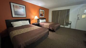 Une chambre d’hôtel avec deux lits, une table de chevet avec une lampe, une porte avec un porte-serviettes et une fenêtre avec des rideaux.