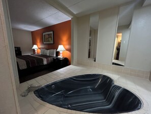 Un cuarto de hotel con una tina de hidromasaje negra grande, una cama con una manta a rayas marrón y blanca, dos lámparas de noche y un cuadro en la pared.
