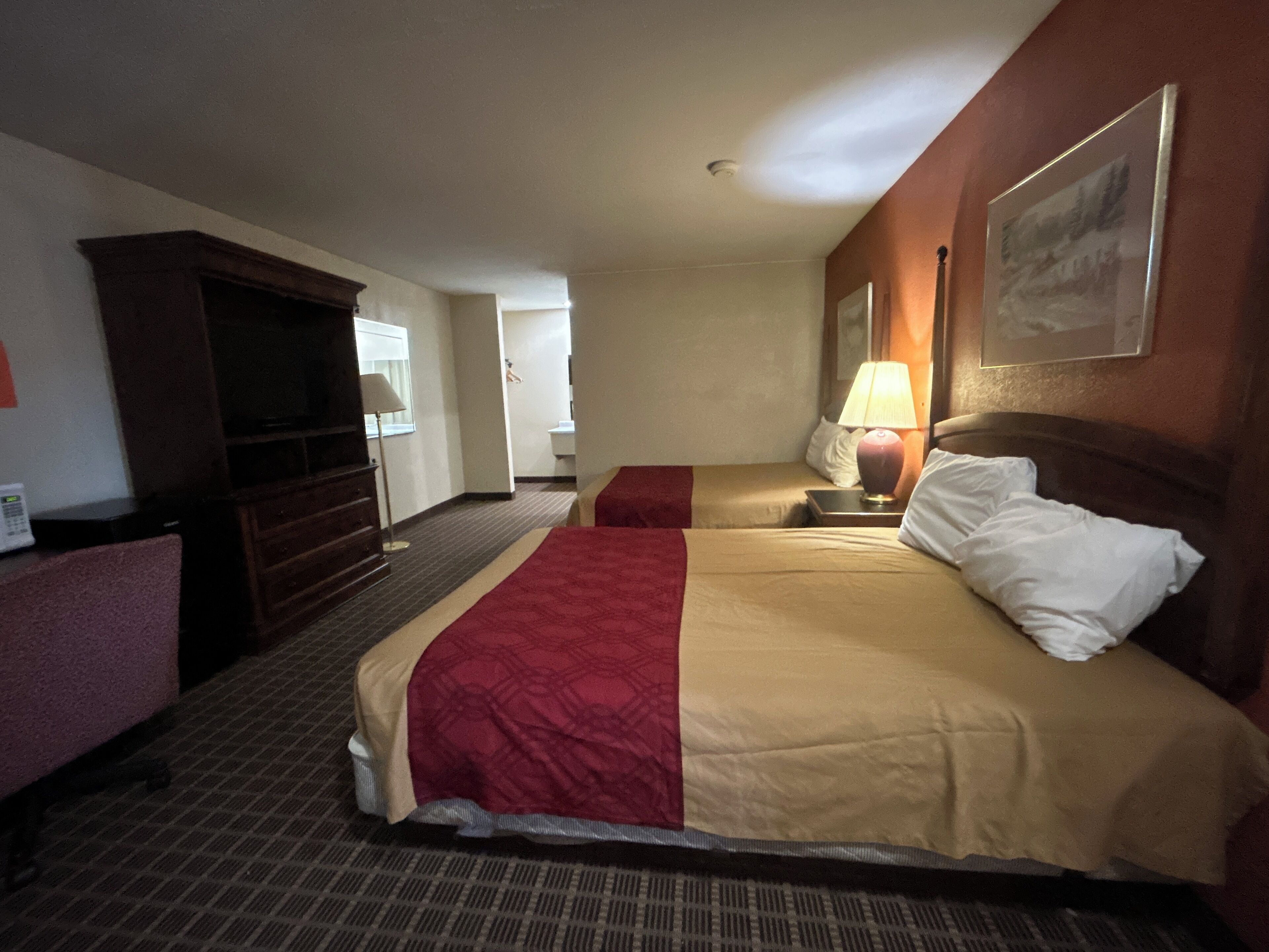 A hotel room with a large bed, a desk with a lamp, a television, and a painting on the wall.