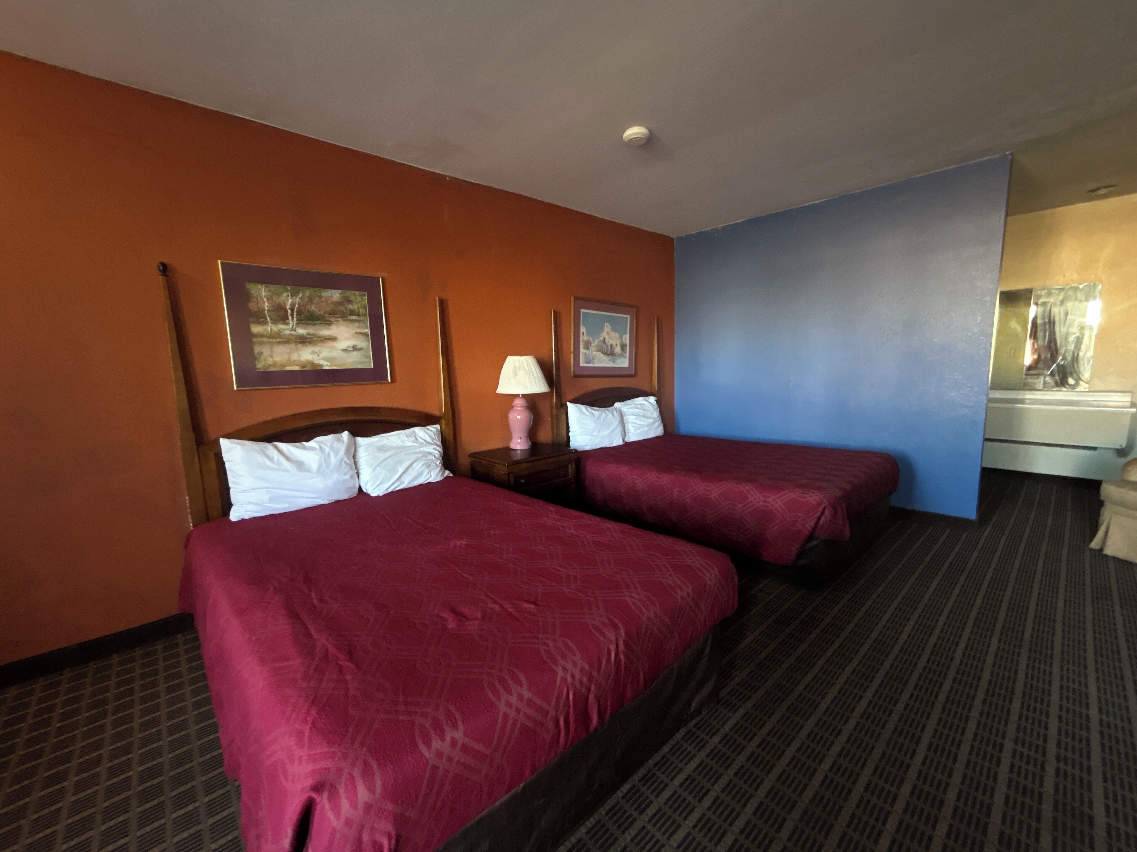 A hotel room with two beds, a nightstand with a lamp, and a dresser.