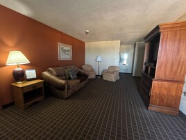 Quarto de hotel com um sofá de couro marrom, duas poltronas, um armário de madeira e uma luminária.