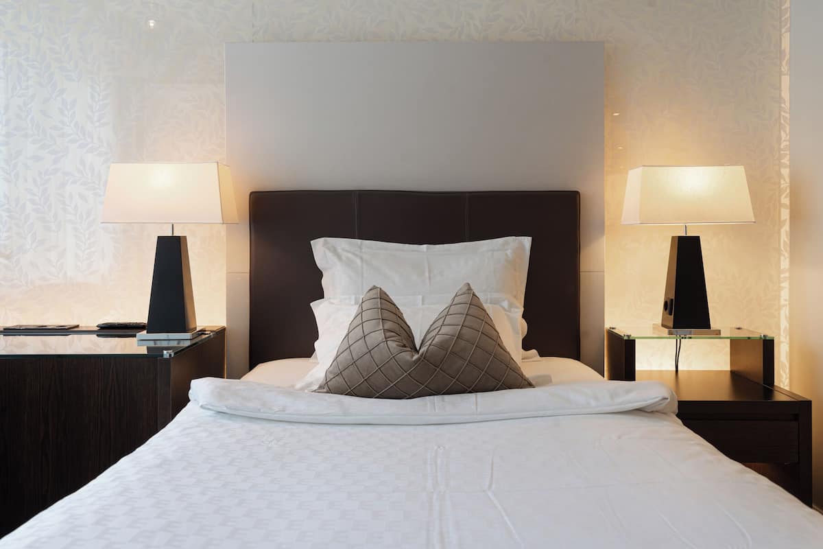 A neatly made bed with two pillows, a dark headboard, and two bedside tables with lamps.