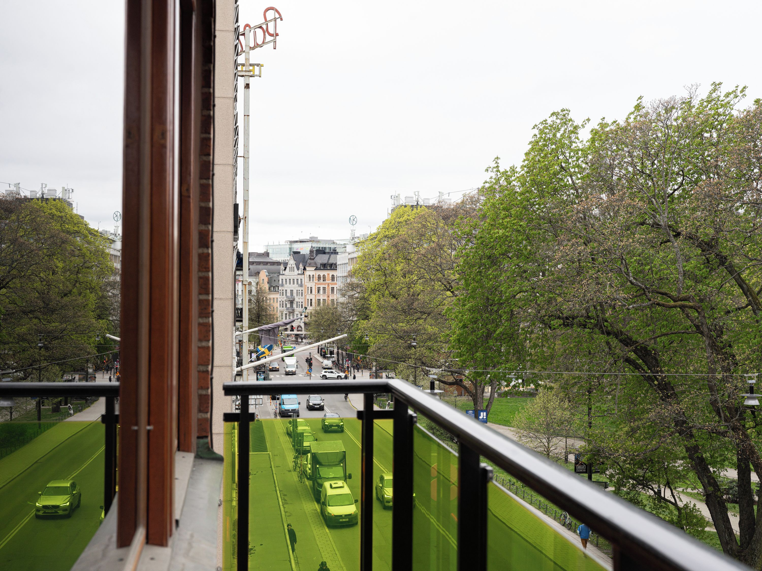 Une vue depuis un balcon donnant sur une rue, avec des voitures et une piste cyclable verte.
