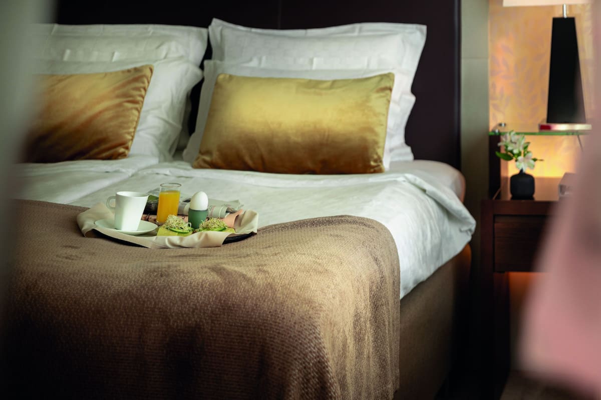 A neatly made bed with a tray of breakfast items, a bedside lamp, and a nightstand with a vase.
