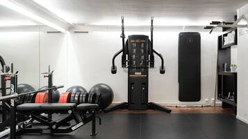 Un gimnasio con un banco de pesas, discos de pesas, una máquina de poleas y un saco de boxeo.