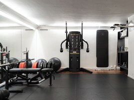A gym with a bench press, weight plates, a cable machine, and a punching bag.