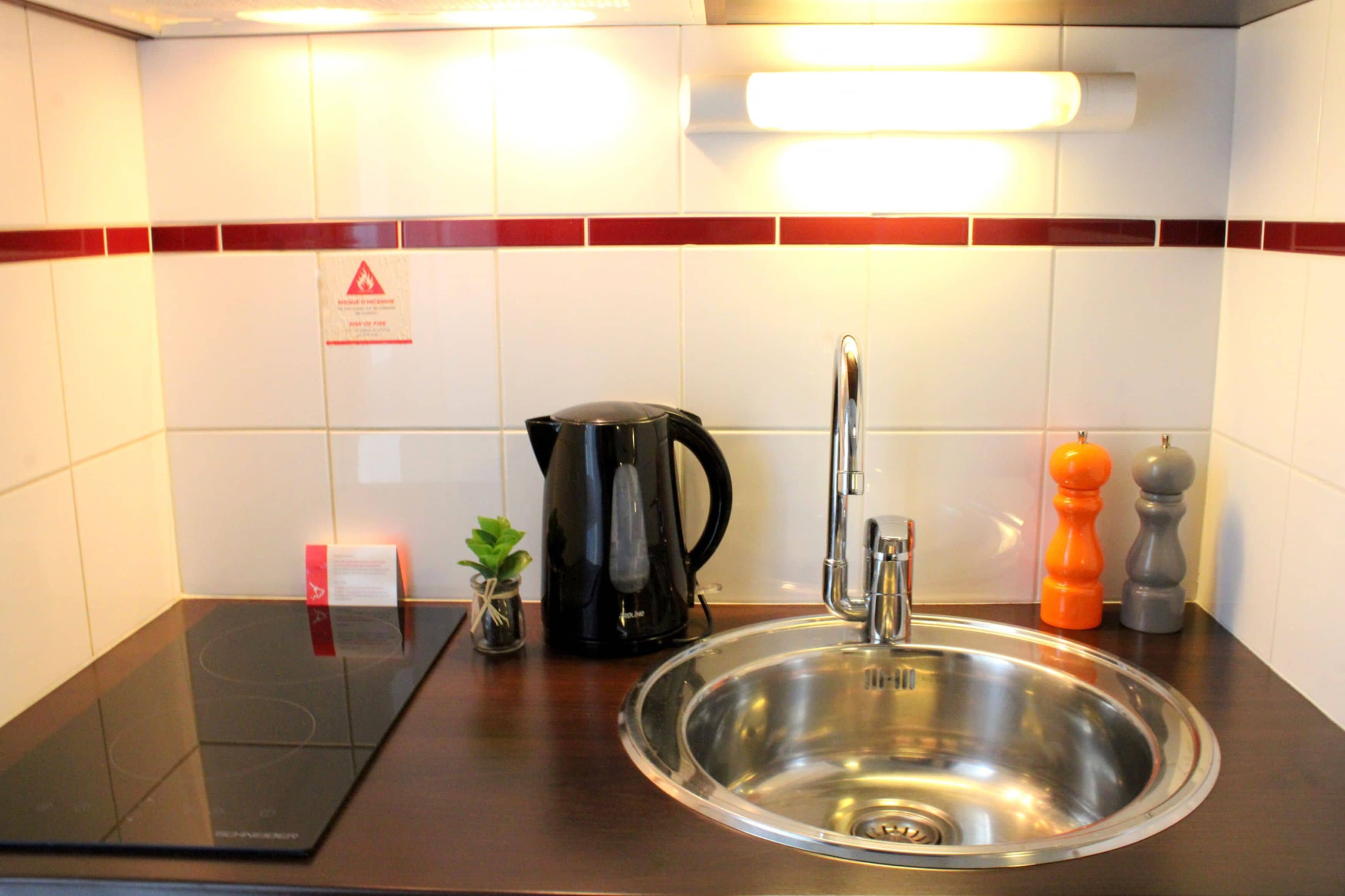 Een moderne keuken met een roestvrijstalen spoelbak, een zwarte elektrische waterkoker en een kleine plant in een pot.