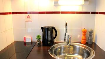 Een moderne keuken met een roestvrijstalen spoelbak, een zwarte elektrische waterkoker en een kleine plant in een pot.