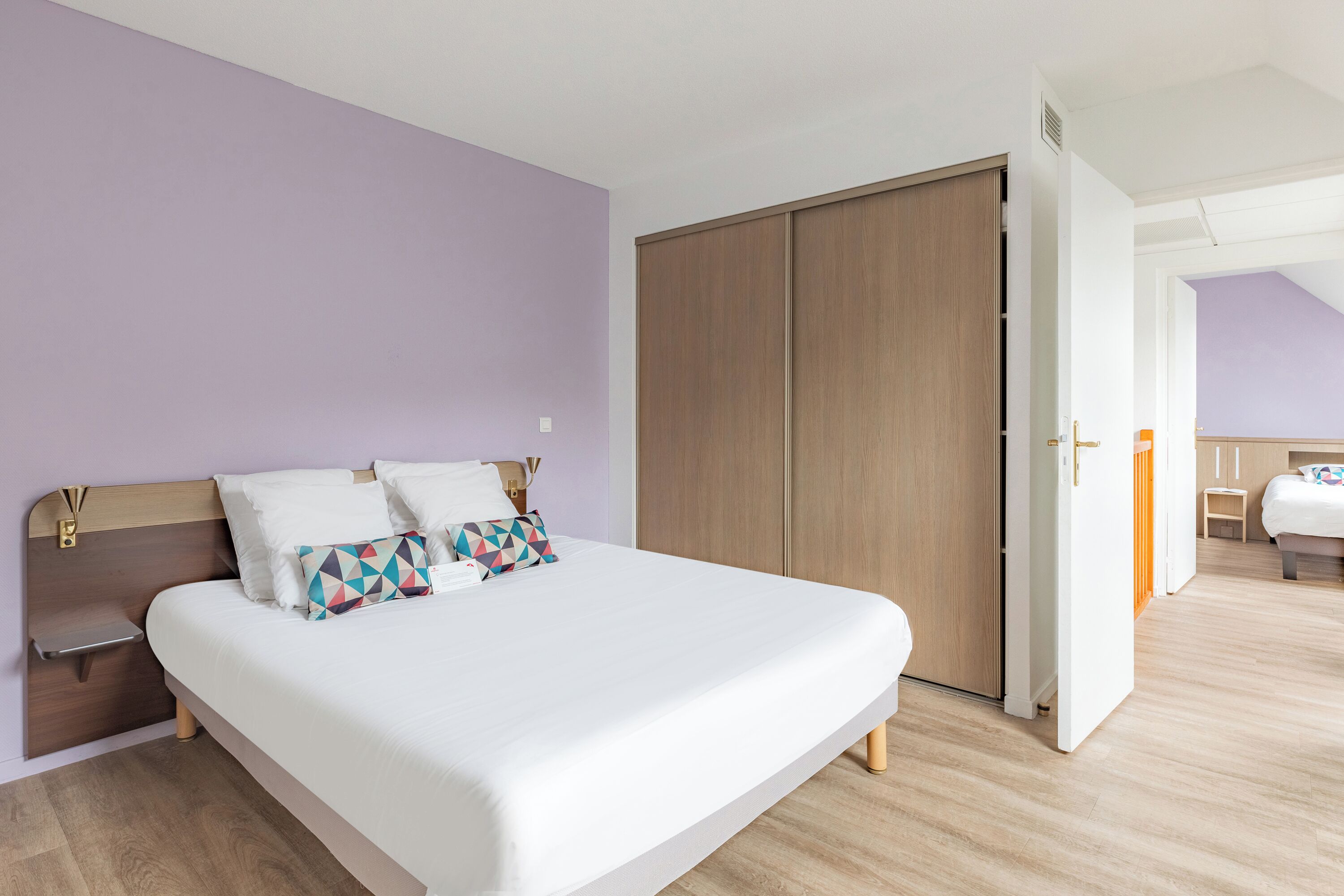 Un dormitorio con cama, mesita de noche, armario y una puerta que da a otra habitación.
