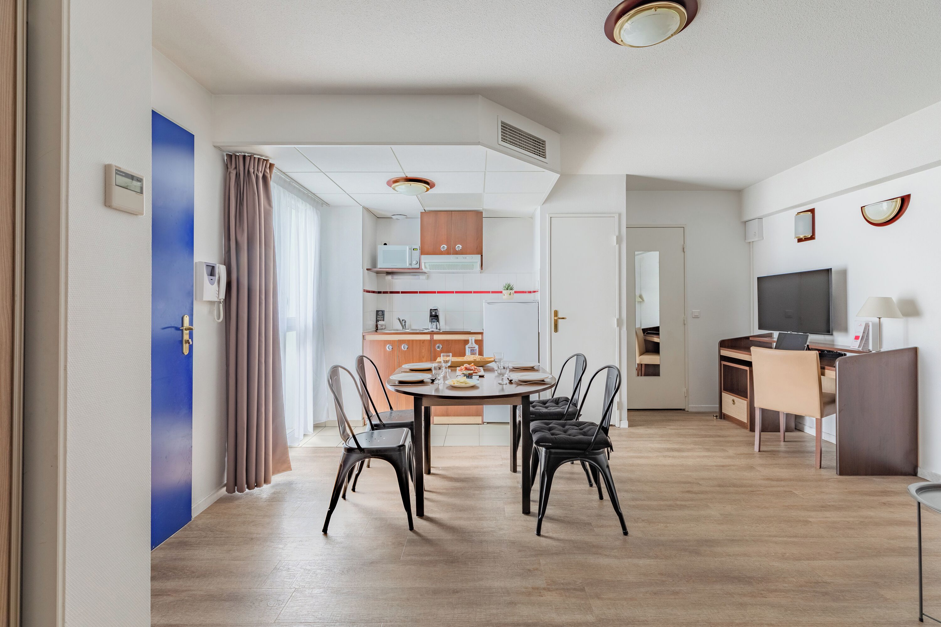 A modern kitchen with a dining area, featuring a round table, chairs, and a TV.