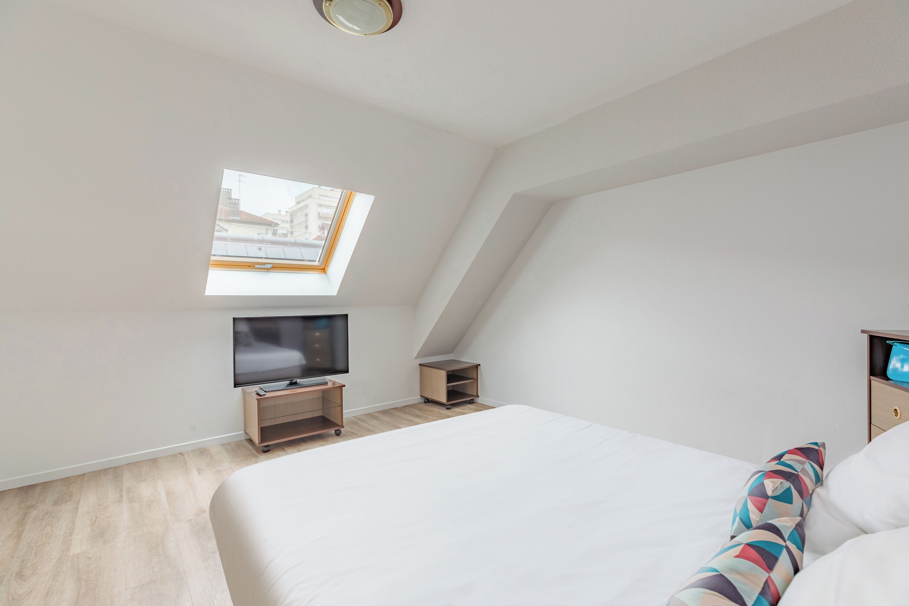 A modern bedroom with a skylight, a bed, a TV, and a small wooden cabinet.