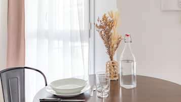 Una mesa de comedor con un plato, un vaso y una botella, una silla y una ventana con cortinas traslúcidas.